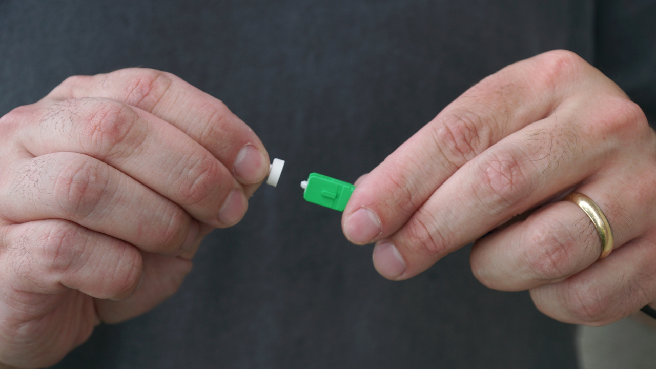 Close-up of hands removing a protective cap from a green fiber-optic connector.