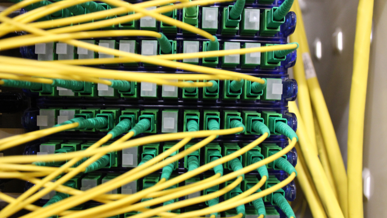 Close-up of yellow fiber-optic cables connected to green ports in a network patch panel.