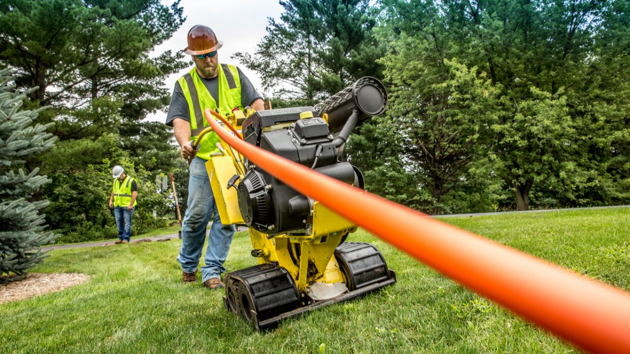 Contractor using a machine to pull orange fiber conduit.